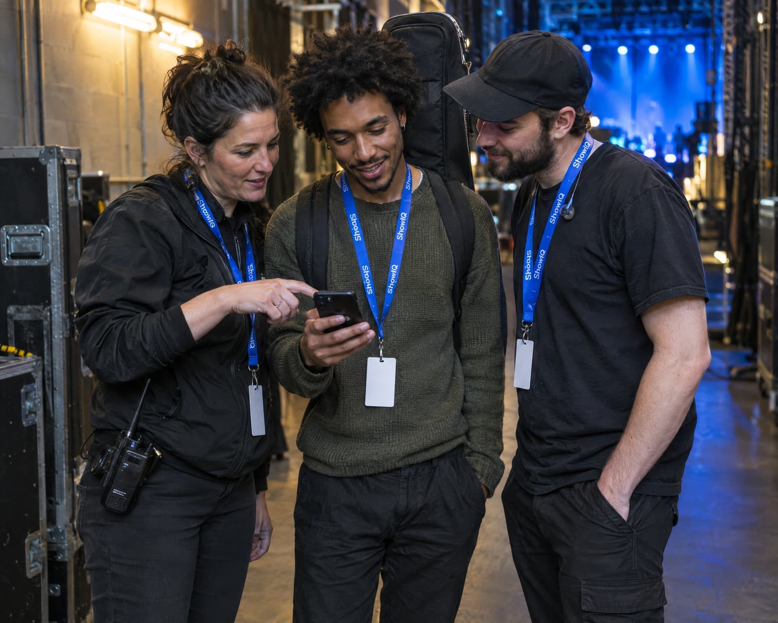 A production manager, an artist and a crew member backstage looking at the same phone, each with their accreditation on a lanyard