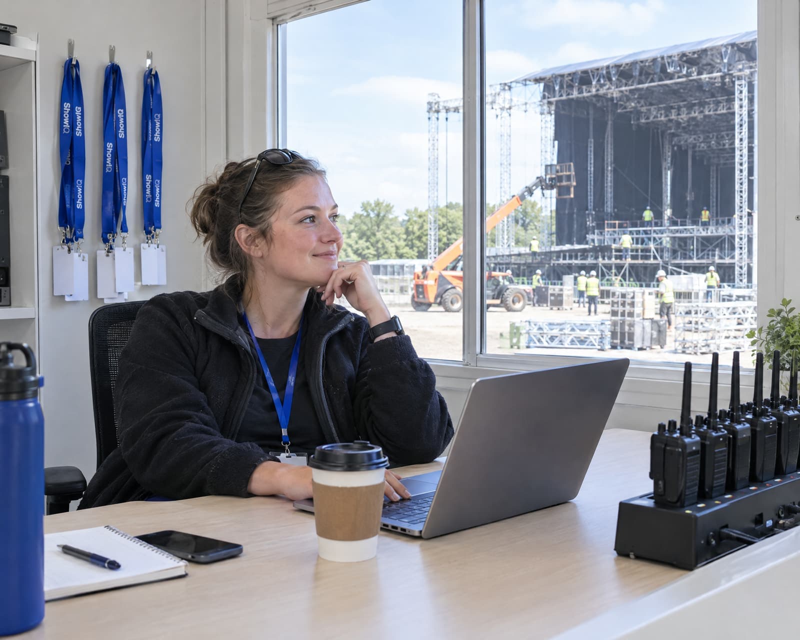 A production coordinator in the festival office during build-up week, the main stage going up outside